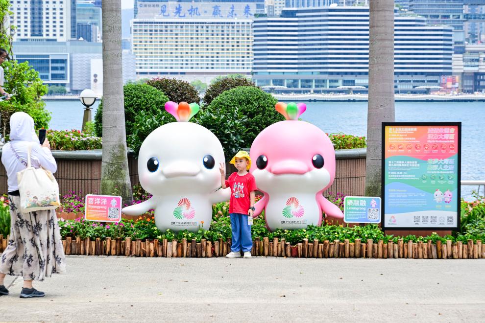 圖為一名兒童在香港金紫荊廣場(chǎng)的第十五屆全國(guó)運(yùn)動(dòng)會(huì)吉祥物旁留影