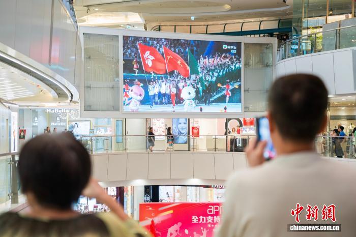 11月9日晚，香港市民在觀塘的一家商場內(nèi)通過大屏幕觀看在廣州舉行的第十五屆全國運動會開幕式。圖為大屏幕顯示出粵港澳三地運動員代表團一同入場。　中新社記者 侯宇 攝