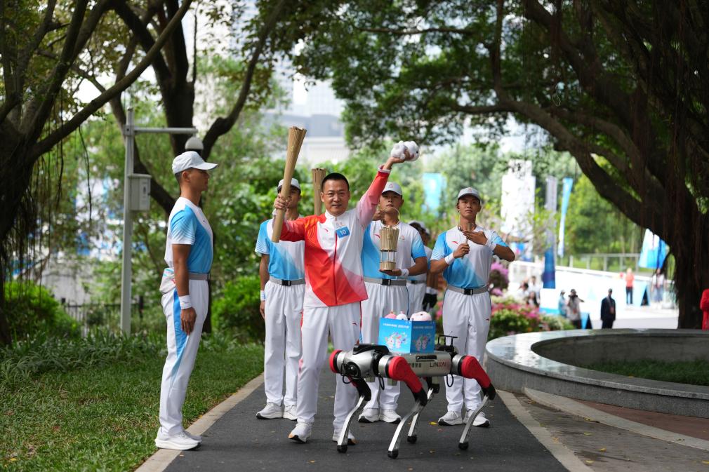 11月2日，火炬手蘭小軍（左二）在火炬傳遞深圳站展示從機器狗上取出的本屆全運會吉祥物玩偶。