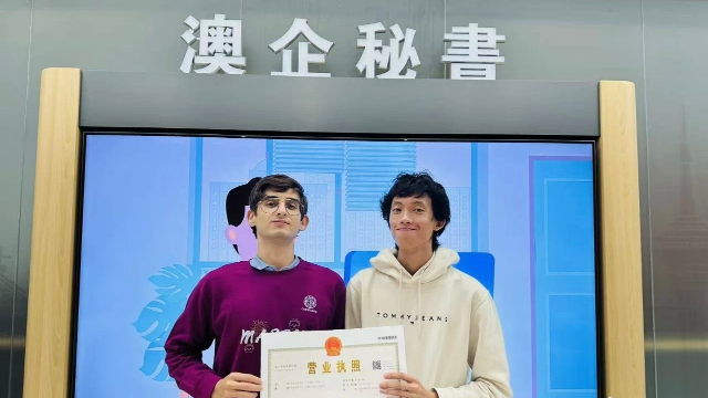 澳門青年陳葦楠與意大利伙伴馬丁在橫琴粵澳深度合作區(qū)政務(wù)服務(wù)中心的“澳企秘書”專窗前并肩而立